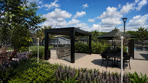 A black metal structure is in the middle of a garden with a table and chairs.