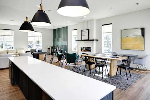 A modern kitchen with a long white island and black pendant lights.