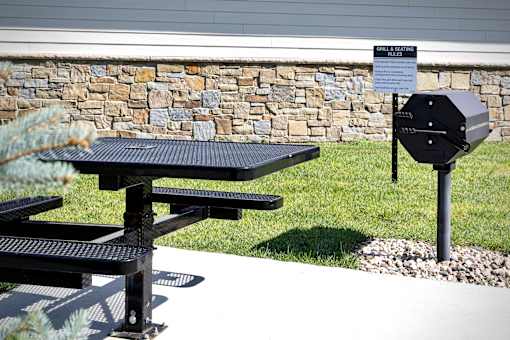 A black grill is on a stand next to a picnic table.