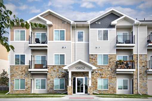 The image shows a modern two-story apartment building with a stone facade and balconies on the upper floor.