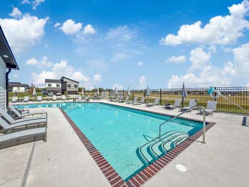 A large swimming pool with lounge chairs and a fence in the background.