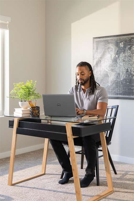 A man with dreadlocks is sitting at a desk using a laptop.