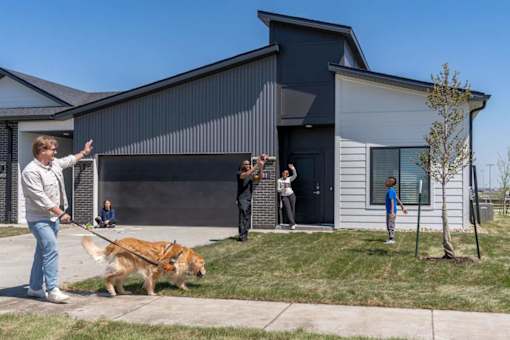 A man is walking his dog in front of a modern house.