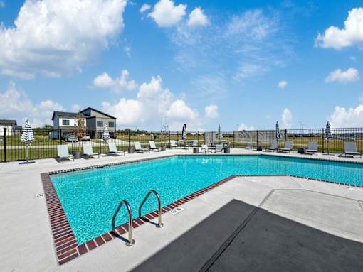 A large outdoor swimming pool with a black fence and a small building in the background.