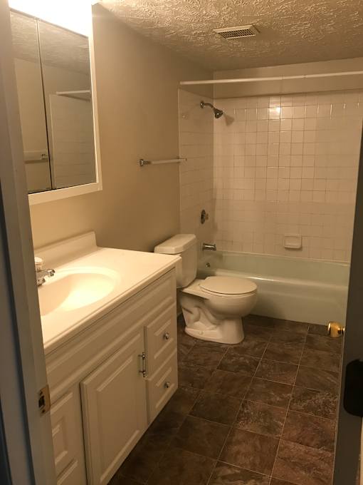A white toilet sits in a bathroom next to a sink and bathtub.