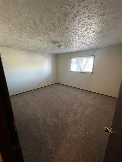 A room with a textured ceiling and carpeted floor.