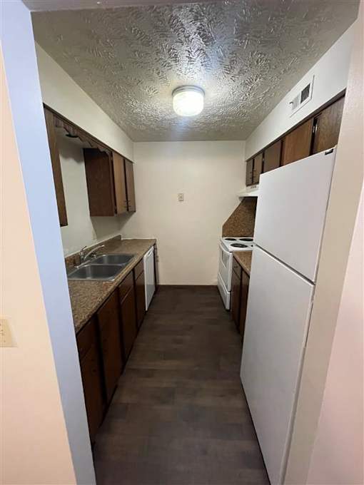 A kitchen with a white refrigerator and brown cabinets.