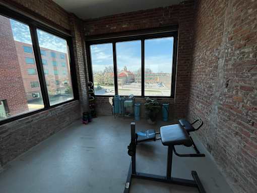 A room with a brick wall and a view of a parking lot through the windows.
