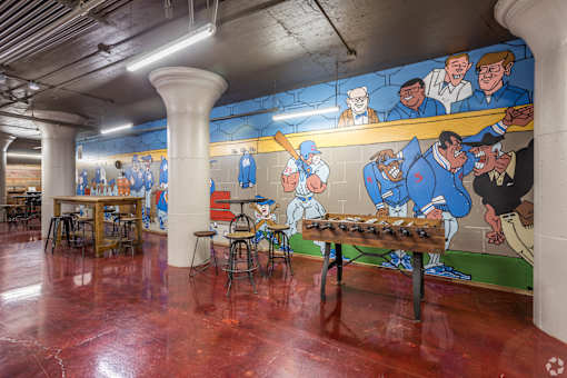 A mural of cartoon men playing baseball is on the wall of a room with tables and chairs.