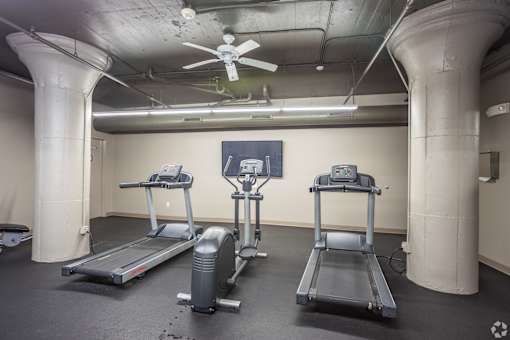 A gym with treadmills, elliptical machines, and a fan.
