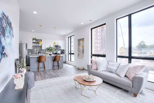 A modern living room with a grey sofa and a kitchen area in the background.
