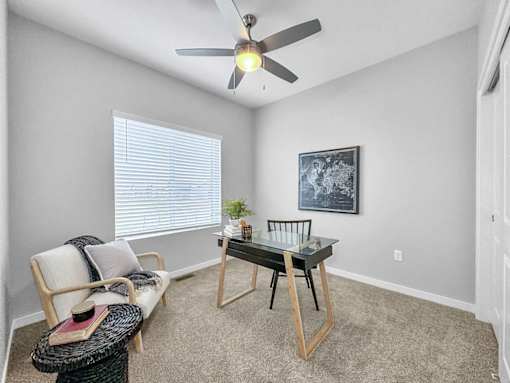 A room with a ceiling fan, a chair, a table, and a painting on the wall.