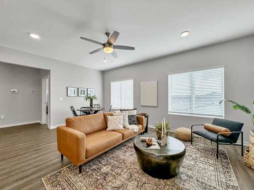 A living room with a brown sofa, a coffee table, and a ceiling fan.