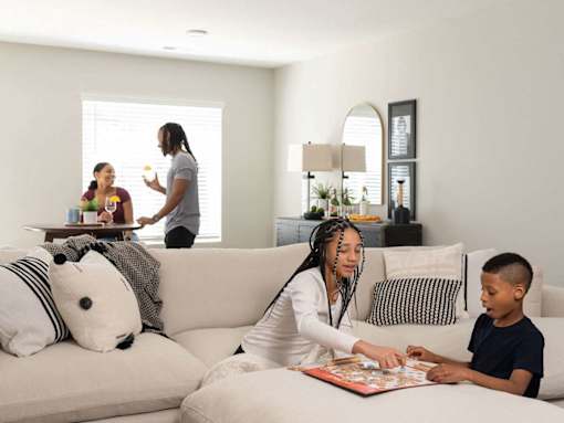 A woman and a boy are playing a board game on a couch in a living room.