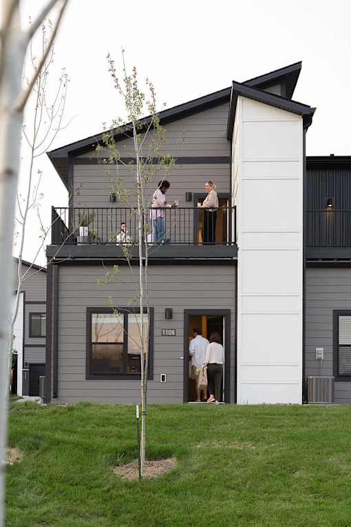 A grey house with a balcony and people standing on it.