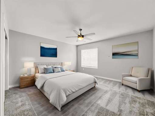 A bedroom with a large bed, a ceiling fan, and a painting on the wall.
