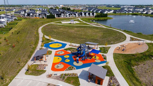 A playground with a slide, swings, and other equipment is surrounded by a grassy area and a body of water.