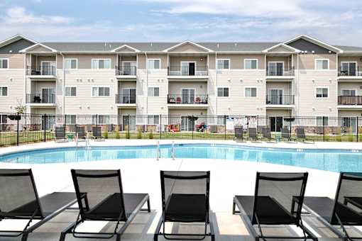 A row of black lounge chairs are arranged in front of a pool at a resort.