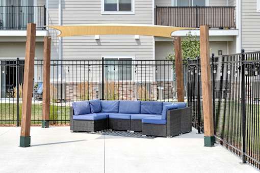 A blue couch is placed on a patio with a black fence.
