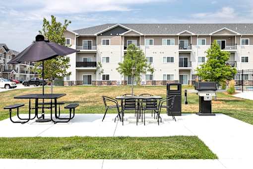 A black umbrella is on a picnic table in front of apartment buildings.