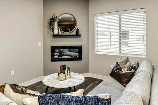 A living room with a grey couch, a round table, and a fireplace.