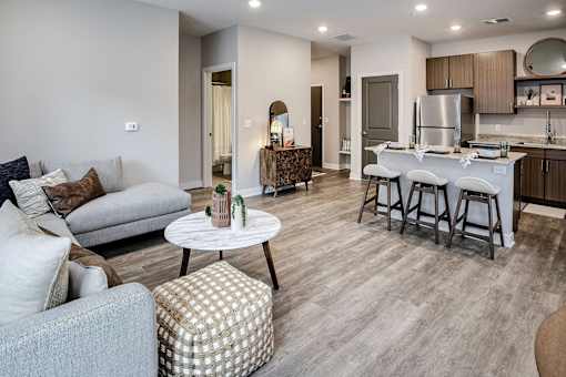 A modern living room with a grey sofa, a white coffee table, and a kitchen area in the background.