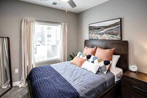 A bedroom with a bed, pillows, a ceiling fan, and a window with curtains.