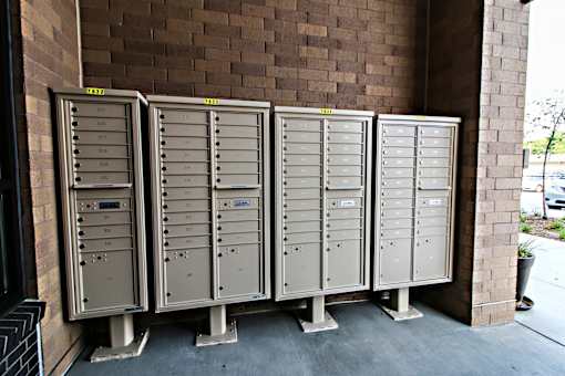 Four large metal mailboxes are lined up against a brick wall.