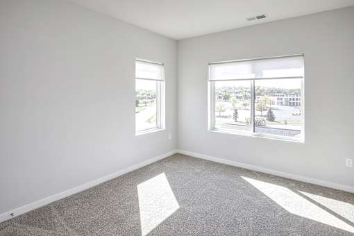 an empty living room with two windows and carpeting