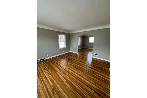 A room with wooden flooring and two windows.