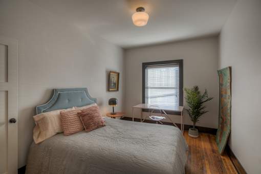 A bedroom with a bed, nightstand, and a plant.