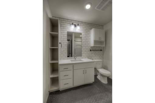 A bathroom with a white toilet, sink, and cabinets.