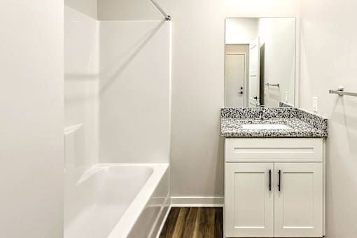 A white bathroom with a marble counter top and a walk in shower.