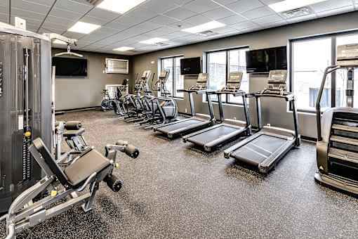 A gym with treadmills, elliptical machines, and a television.