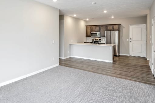 an empty living room with a kitchen in the background