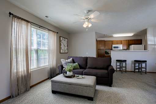 A living room with a brown couch, a grey ottoman, and a ceiling fan.