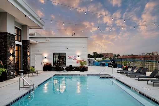 A pool with a building behind it and lights hanging from the roof.