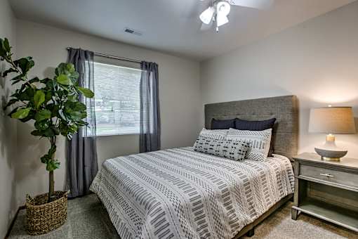 A bedroom with a bed, nightstand, and a potted plant.