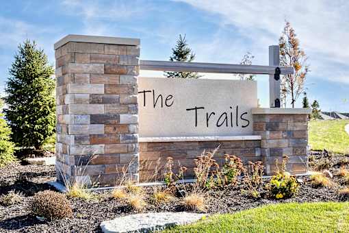 A sign that says "The Trails" is mounted on a stone pillar.