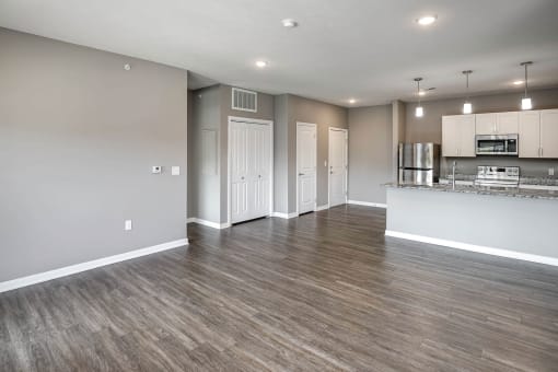 an empty living room with a kitchen in the background