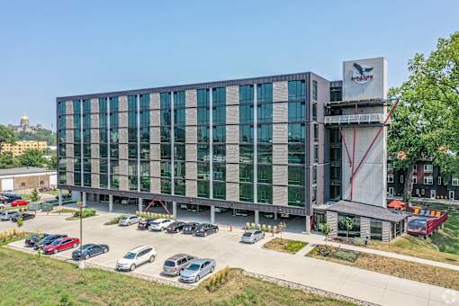 A modern building with a glass facade and a parking lot in front.