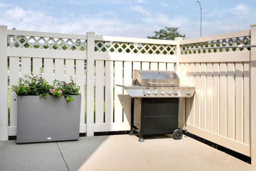 a patio with a grill and a white fence