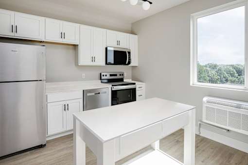 A white kitchen with a refrigerator, microwave, oven, and a table.