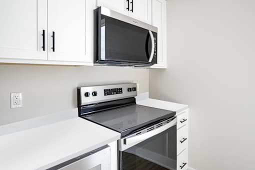 A black microwave oven is mounted on a white cabinet above a stove.