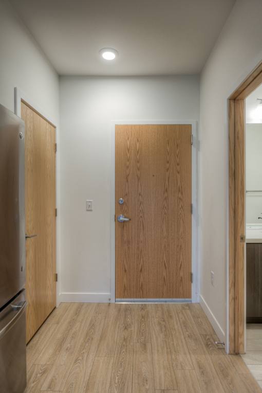 A hallway with a wooden door and a refrigerator on the left.