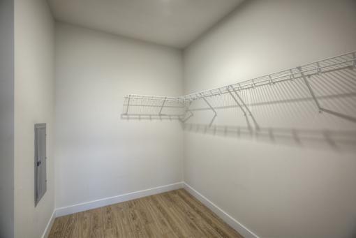 Empty room with a wooden floor and a white wall with a door and a shelf.