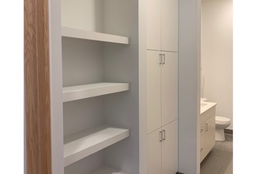 A white bathroom with a toilet and a shelving unit.