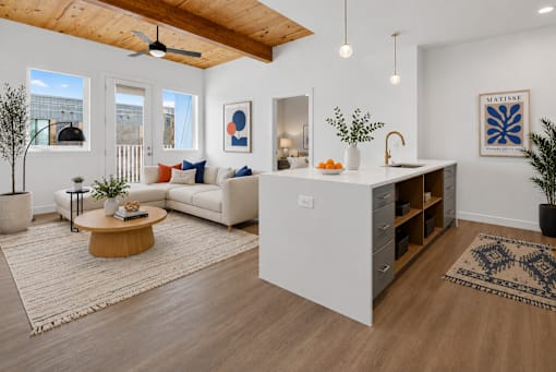 A modern kitchen with a white island and a white couch with orange pillows.