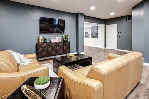 VUE 19 (Clubhouse) - Lounge with a brown leather couch, a black coffee table, and a flat screen TV mounted on the wall.
