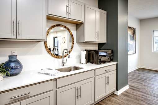 Vue 19 - Kitchen with white cabinets and a round mirror above the sink.